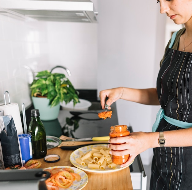 Женщина, стоящая на кухонном столе, ставя макаронный соус в банку