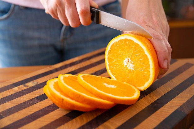 Woman standing near table and cutting orange on slices