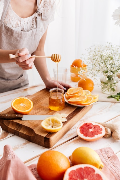 Woman standing near table with citruses and holding honey.