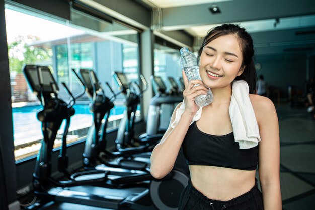 Woman standing and relaxing after exercising, holding a bottle of water to touch the face.