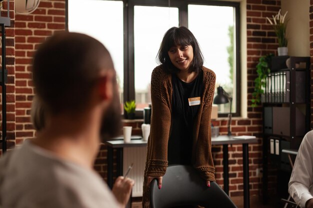 Woman standing and talking about progress with people at aa therapy meeting, sharing success with group at rehab session. Person having conversation with patients and psychotherapist.