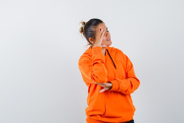 woman standing in thinking pose in orange hoodie and looking dreamy