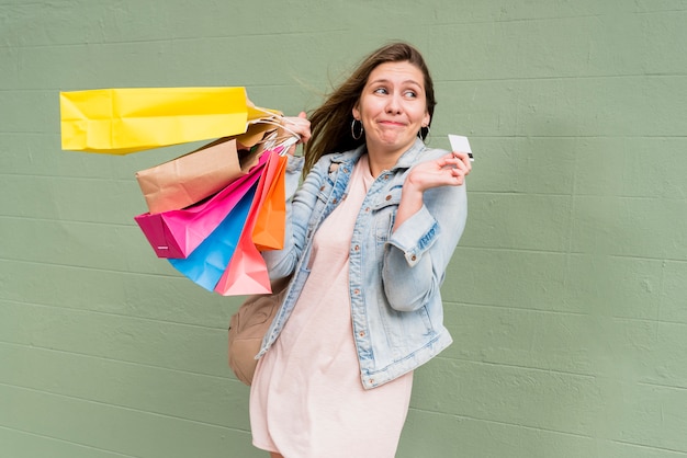 Woman standing with credit card and shopping bags at wall 
