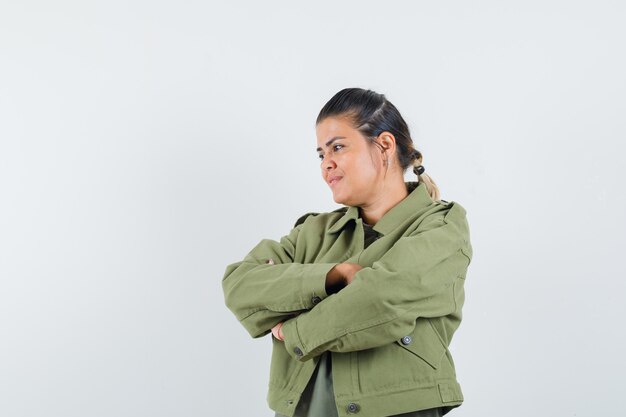 Woman standing with crossed arms in jacket, t-shirt and looking pensive