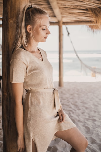 Woman standing next to a wooden column on sand