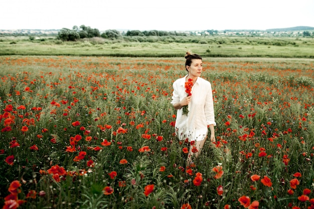 Woman stands holding a poppies flower bouquet, among the meadow of poppies