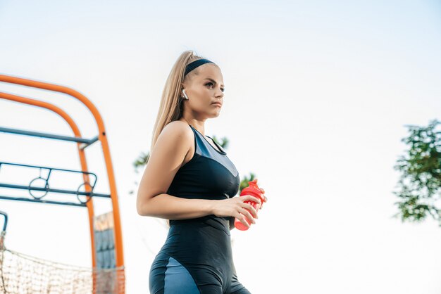 Woman stands at the outdoor gym with a bottle of water