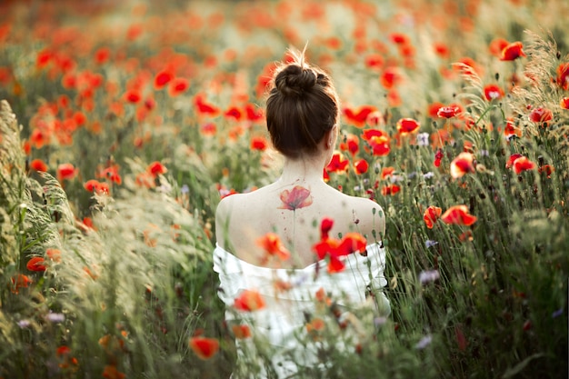 女性は裸の背中で立って、ケシ畑の中で入れ墨の花ポピーがあります