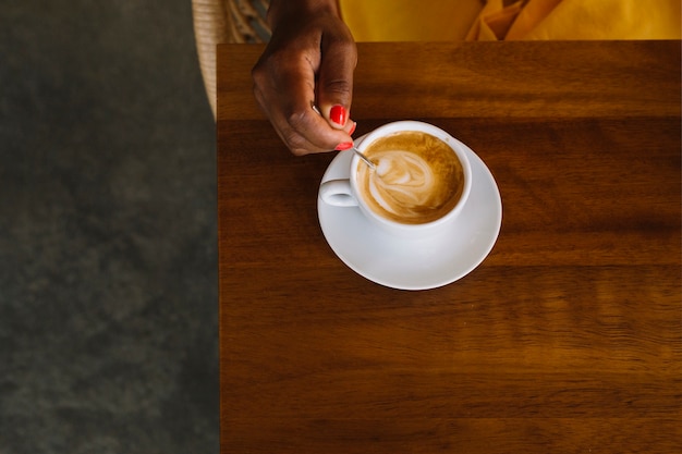 A woman stirring hot coffee with spoon on wooden table