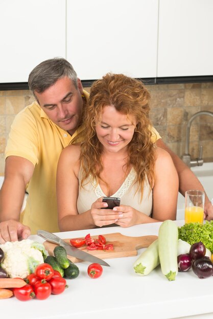 Woman stopped cooking to read the message in her mobile phone. Man is behind her looking at the phone.