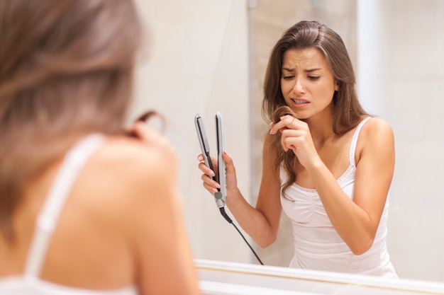 Женщина, выпрямляющая волосы в ванной комнате
