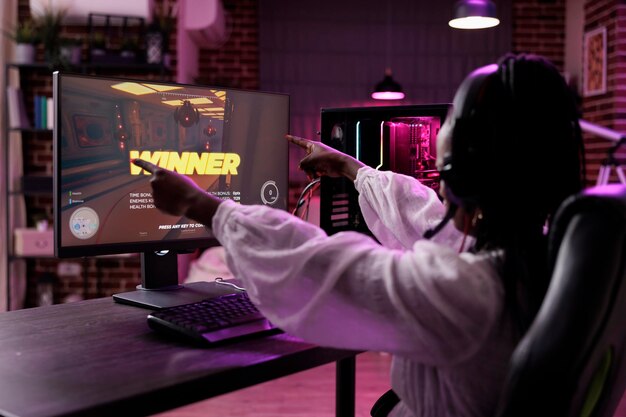 Женщина-стример играет в турнир по видеоиграм на компьютере, празднуя победу. Женщина-игрок выигрывает чемпионат по играм в жанре экшн, развлекается онлайн-соревнованиями по геймплею на ПК.