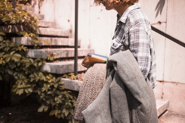 Женщина в уличной одежде с книгами и шарфом в руке возле шагов