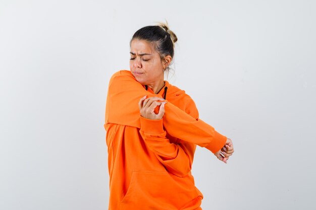 Woman stretching arm in orange hoodie and looking pensive