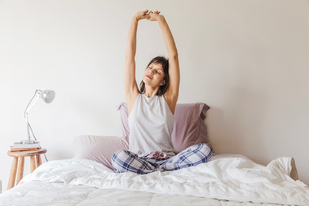 Woman stretching arms on bed in the morning