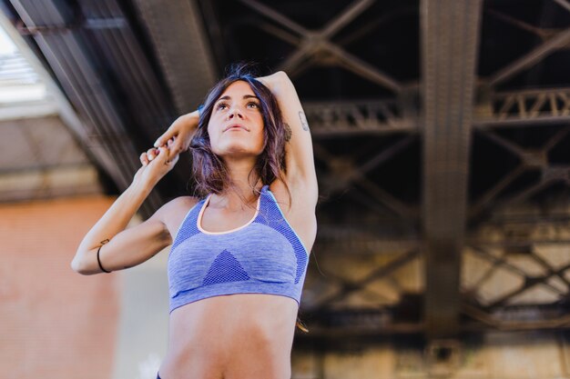 Woman stretching arms standing under bridge