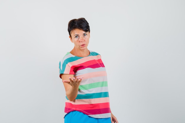Free photo woman stretching hand in puzzled gesture in striped t-shirt, pants