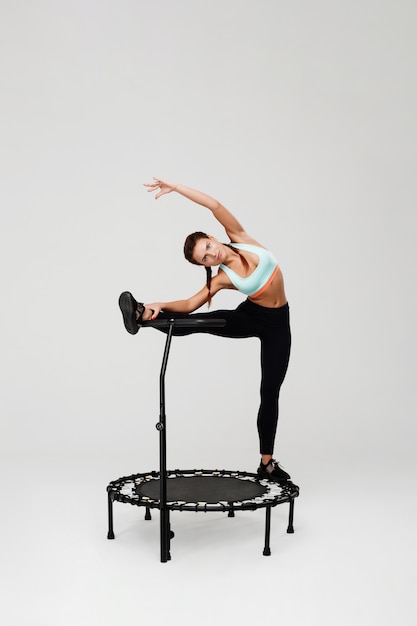 Woman stretching muscles staying on rebounder with leg on handle