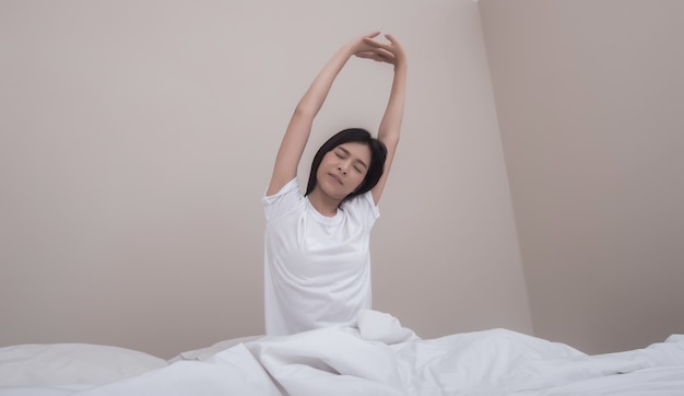 Woman stretching with closed eyes sitting on bed