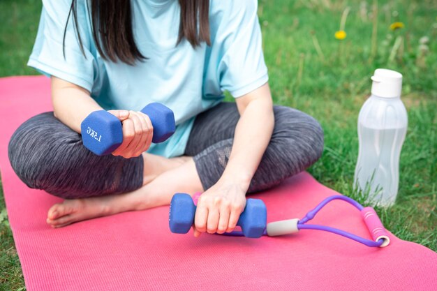 Woman stretching with dumbbells doing fitness exercises in green park