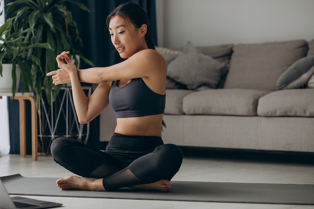 Женщина, растягивающаяся на коврике для йоги дома