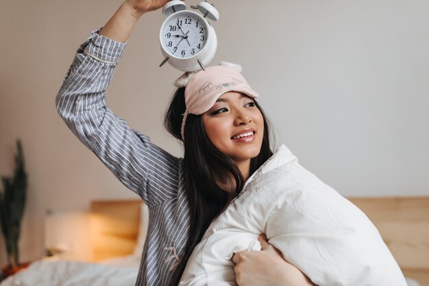 woman in striped pajamas holding huge white alarm clock