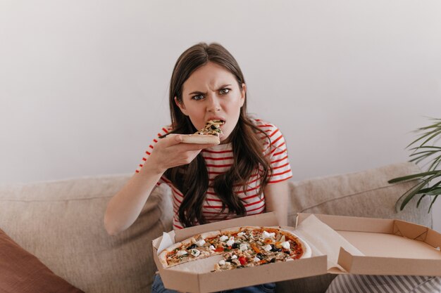 woman in striped shirt with hungry look bites fresh pizza