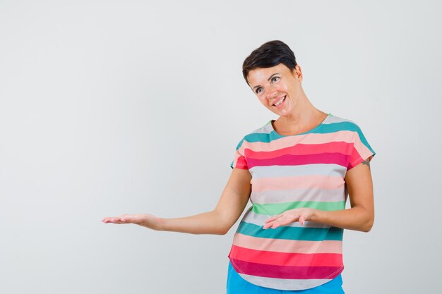 Woman in striped t-shirt showing something or welcoming and looking gentle