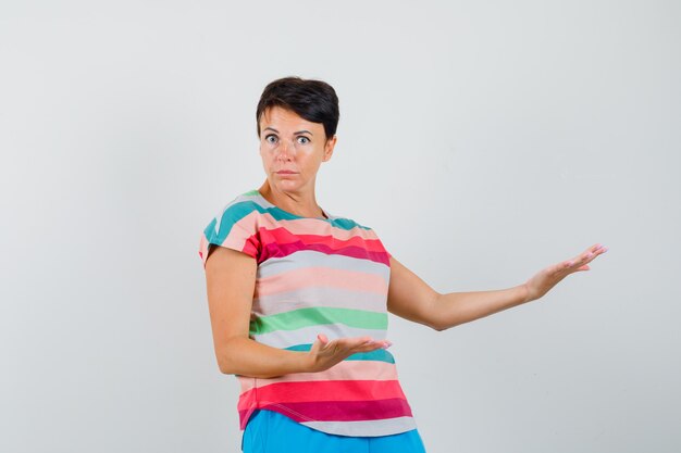 Женщина в полосатой футболке показывает что-то или приветствует и выглядит озадаченным