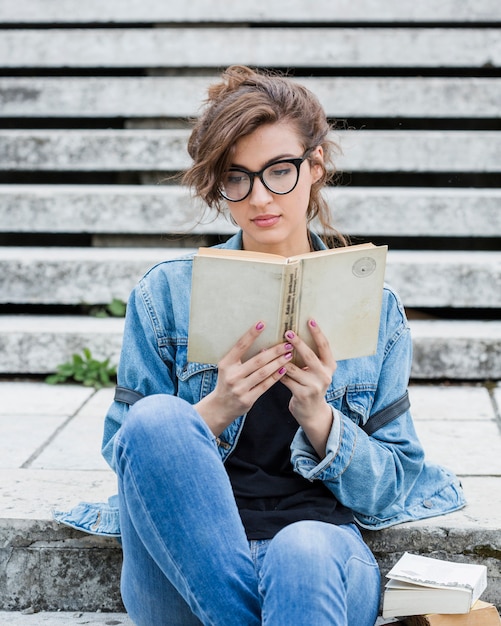 Woman student reading book on park stairs