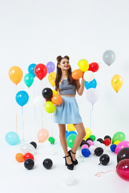 Woman in stylish outfit posing with balloons at bright party