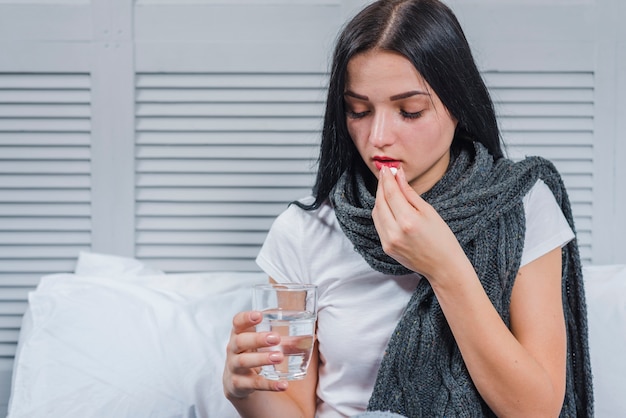 Free photo woman suffering from cold holding glass of water taking medicine