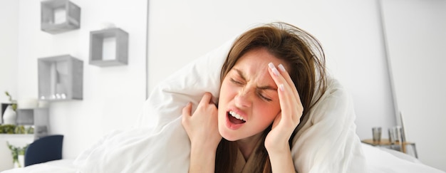 Бесплатное фото Женщина с головной болью утром лежит в постели под одеялом и кричит от боли в голове