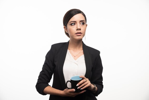 A woman in a suit with a cup of coffee in hand on white wall.