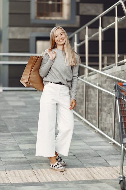 Foto gratuita donna in una città estiva. signora con borse marroni. donna in un maglione grigio.