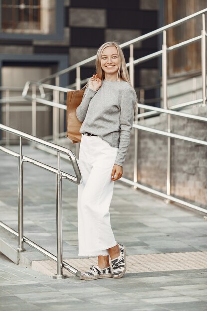 Woman in a summer city. Lady with brown bags. Woman in a gray sweater.