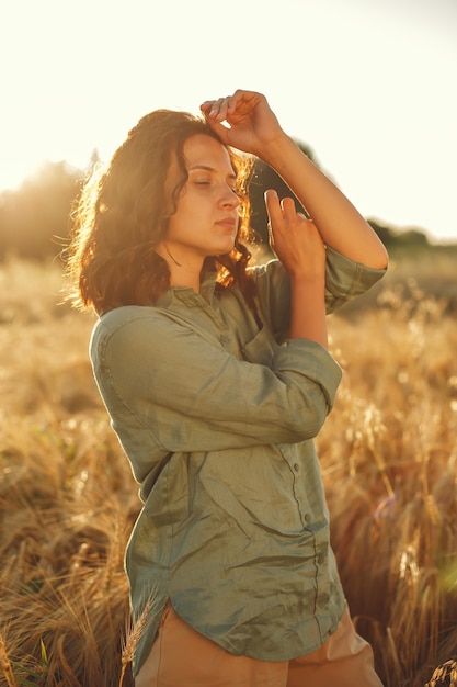 Free photo woman in a summer field. brunette in a green shirt. girl on a sunset background.