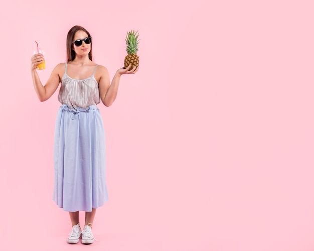 Woman in sunglasses holding glass of juice and pineapple 