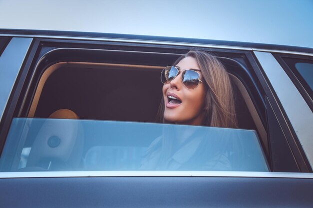 A woman in sunglasses looking through car's window.