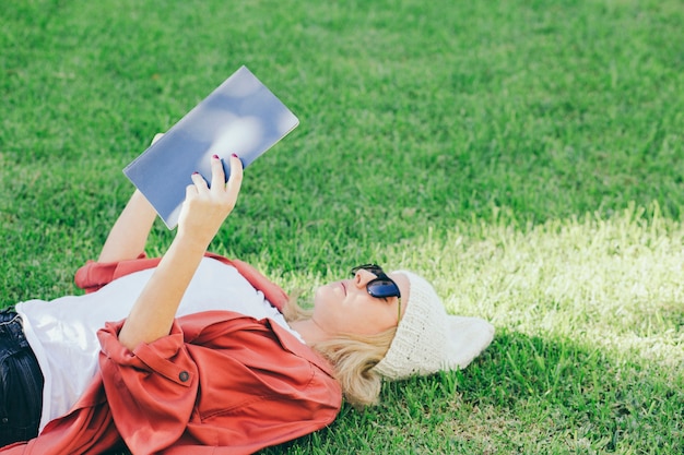 Free photo woman in sunglasses reading book on lawn