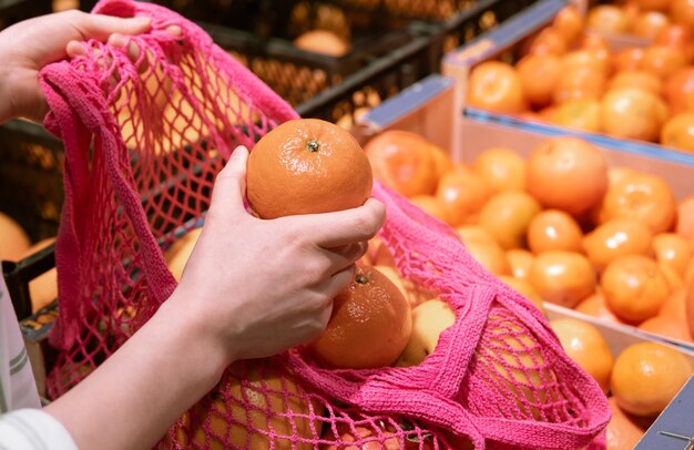 A woman in a supermarket puts oranges in a shopping bag