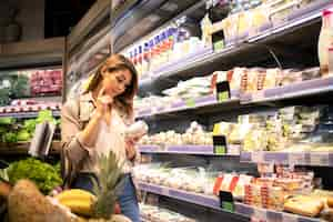 Free photo woman in supermarket reading nutrition values from a product by the shelf