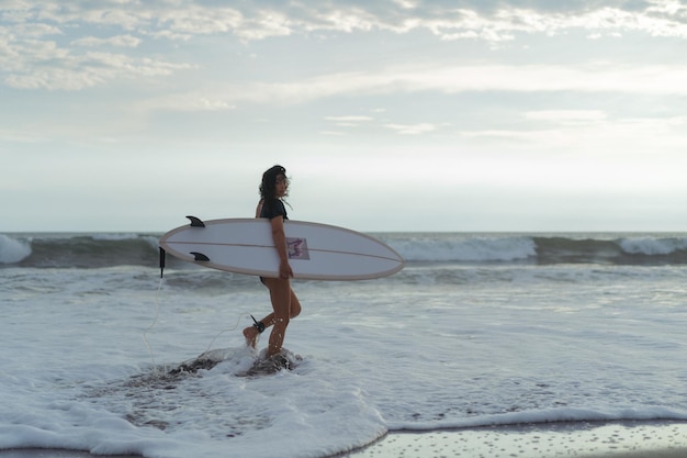 Woman surfer with surfboard on the ocean at sunset