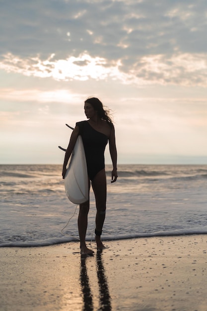 日没時に海にサーフボードを持つ女性サーファー