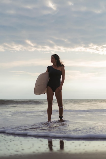 Woman surfer with surfboard on the ocean at sunset