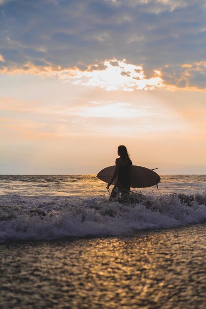 日没時に海にサーフボードを持つ女性サーファー