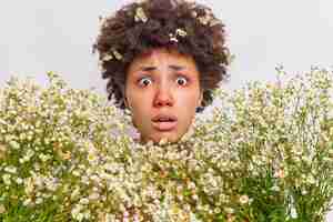 Foto gratuita la donna circondata da camomilla ha una reazione allergica agli sguardi dei fiori di campo ha gli occhi gonfi e rossi posa su bianco