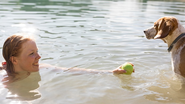 Woman swimming and playing with dog side view