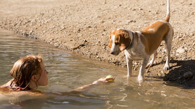 海岸に座っている犬と一緒に泳いだり遊んだりする女性
