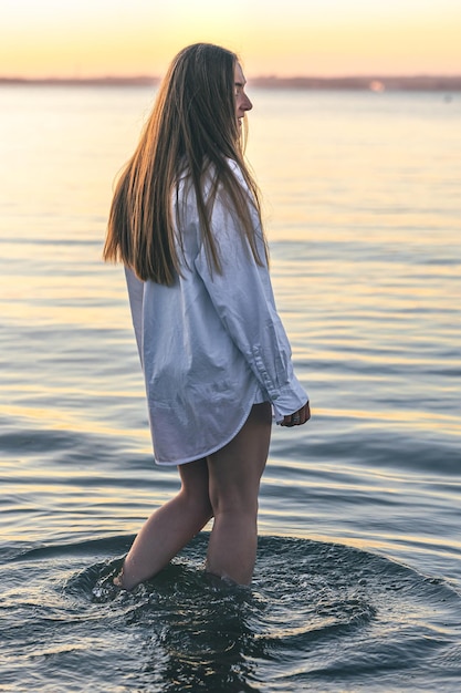 A woman in a swimsuit and a white shirt in the sea at sunset